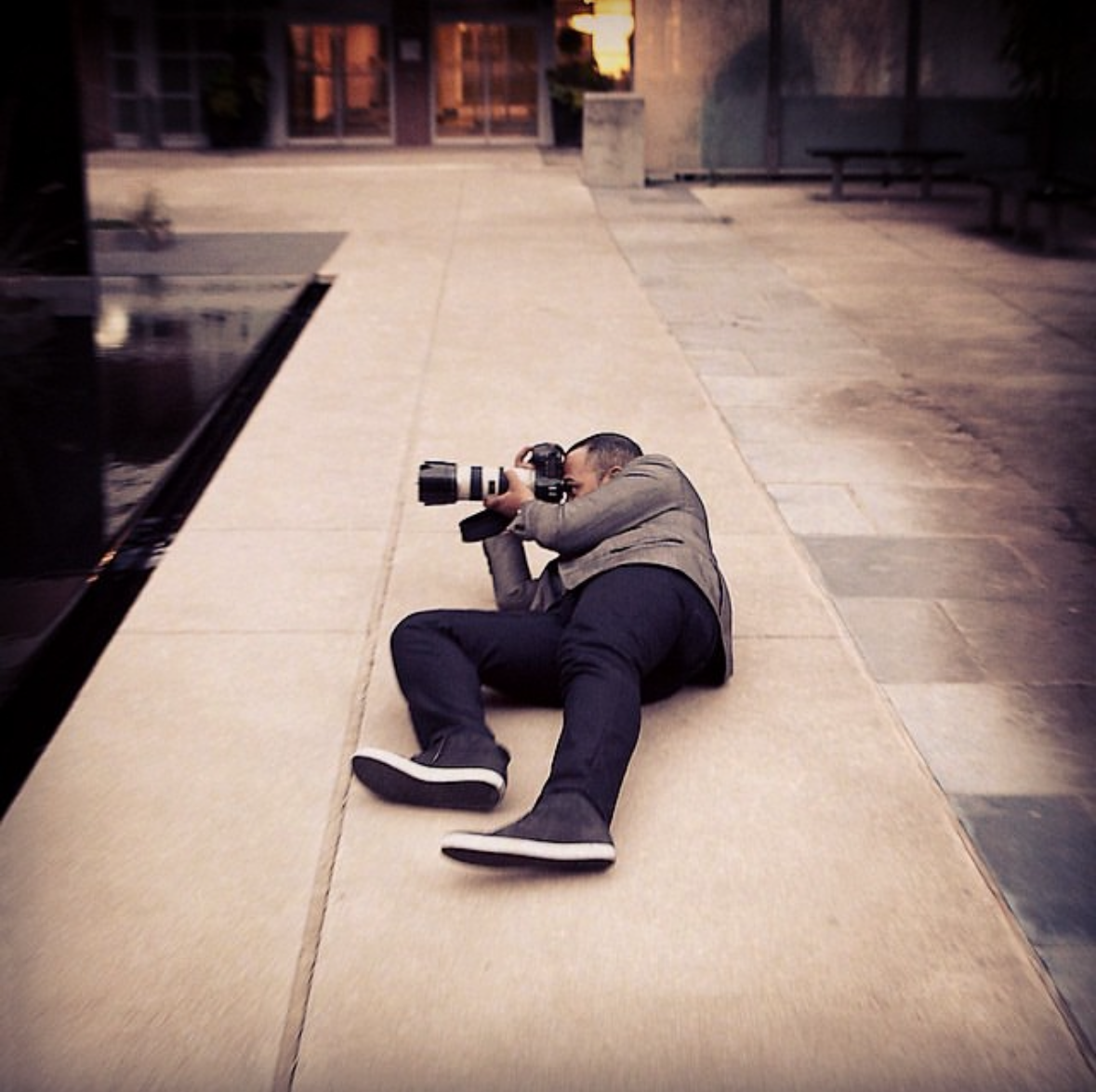 Mark Anthony lying on a walkway, shooting with a telephoto lens