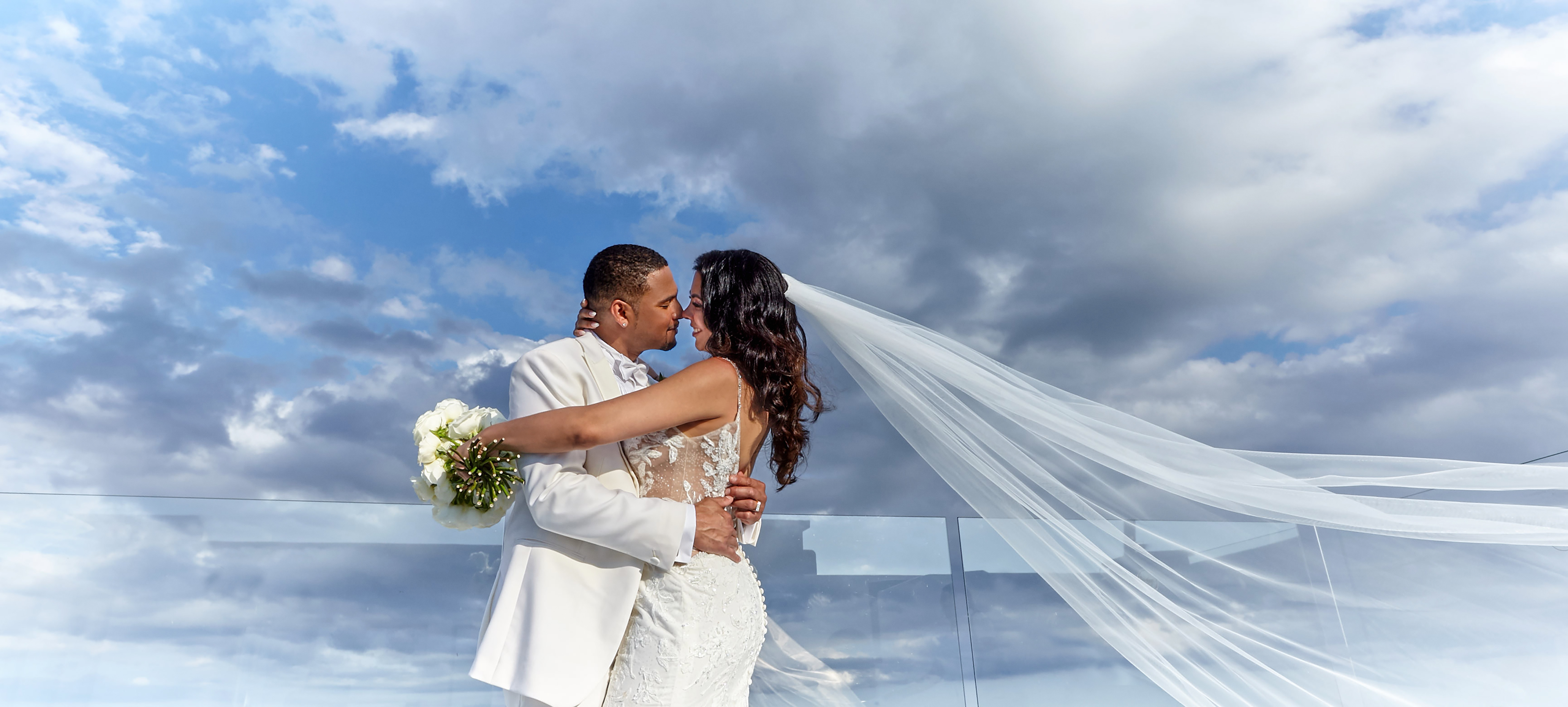Couple embracing against a cloudy sky, veil in the wind